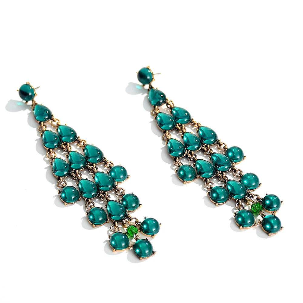 A pair of long tassel drop earrings with green transparent resin crystals arranged in a cascading design.