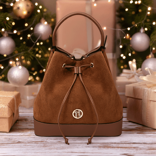 Luxurious Minerva Suede Leather Bucket Bag in cognac with gold-tone logo and drawstring detail, styled among festive gift boxes and warm holiday lights by Montipi.
