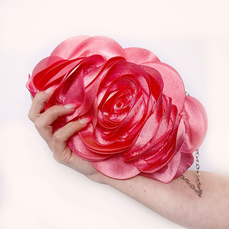 An elegant close-up of hands holding the Rose Chic Petal Clutch in a Couture pose. A delicate rose-shaped clutch bag with layered petal detailing in a soft, romantic hue. The elegant floral design mimics the texture of blooming petals, creating a timeless statement piece. Set against a refined backdrop, the clutch exudes femininity and sophistication, perfect for weddings, cocktail events, and special occasions. Rose Chic Petal Clutch Bag in rose pink by Montipi Australia