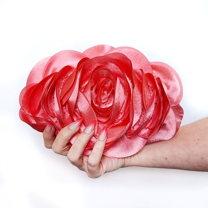 An elegant close-up of hands holding the Rose Chic Petal Clutch in a front view Couture pose. A delicate rose-shaped clutch bag with layered petal detailing in a soft, romantic hue. The elegant floral design mimics the texture of blooming petals, creating a timeless statement piece. Set against a refined backdrop, the clutch exudes femininity and sophistication, perfect for weddings, cocktail events, and special occasions. Rose Chic Petal Clutch Bag in rose pink by Montipi Australia