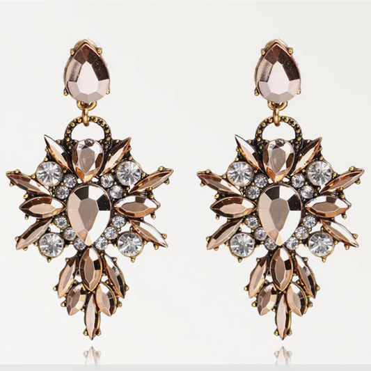 Pair of ornate earrings with rose gold and clear gemstones on a white background