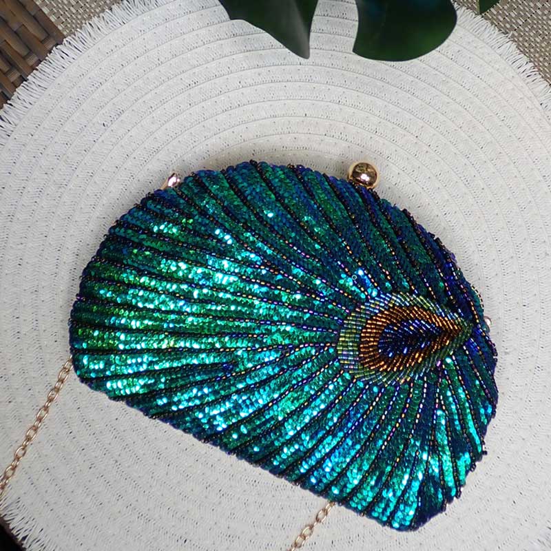 Elegant Teal Sequin Peacock Clutch Bag with glimmering sequins in green teal, gold tone chain strap and hasp closure in refined tropical chic background with white matte and monstera leaf, inspiring aesthetic photography created by Montipi Australia