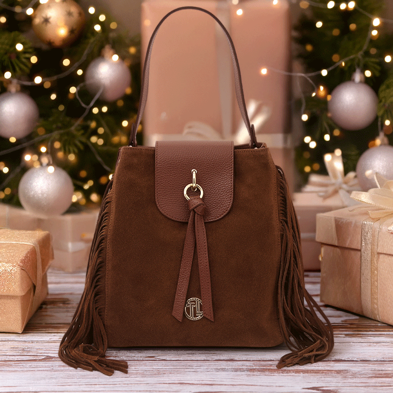 Nomad Suede Leather Fringe Shoulder Bag in brown suede and pebbled leather, styled among festive Christmas gifts and lights – a luxurious boho-luxe holiday gift by Montipi.